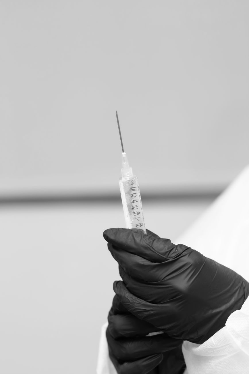 black and white close up of gloved hand holding syringe